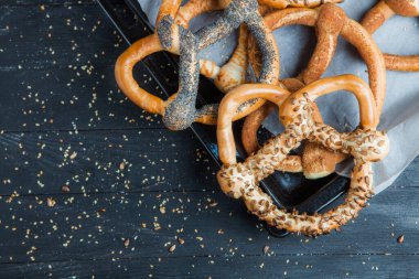 Taze ev yapımı yumuşak krakerler. Siyah arka planda tohumları olan farklı pişmiş simit türleri..