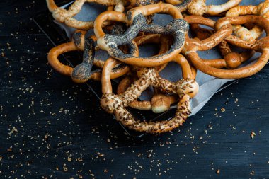 Taze ev yapımı yumuşak krakerler. Siyah arka planda tohumları olan farklı pişmiş simit türleri..