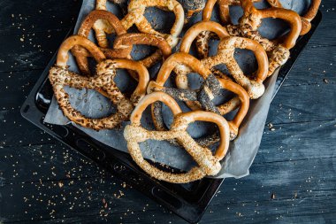 Taze ev yapımı yumuşak krakerler. Siyah arka planda tohumları olan farklı pişmiş simit türleri..