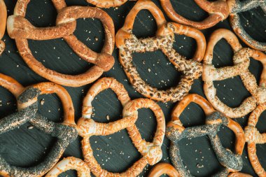 Taze ev yapımı yumuşak krakerler. Siyah arka planda tohumları olan farklı pişmiş simit türleri..