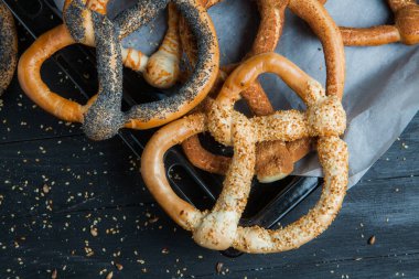 Taze ev yapımı yumuşak krakerler. Siyah arka planda tohumları olan farklı pişmiş simit türleri..