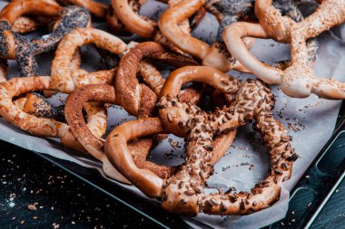 Taze ev yapımı yumuşak krakerler. Siyah arka planda tohumları olan farklı pişmiş simit türleri..