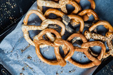 Taze ev yapımı yumuşak krakerler. Siyah arka planda tohumları olan farklı pişmiş simit türleri..