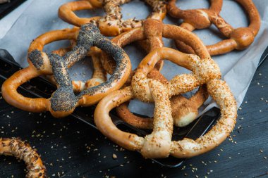 Taze ev yapımı yumuşak krakerler. Siyah arka planda tohumları olan farklı pişmiş simit türleri..