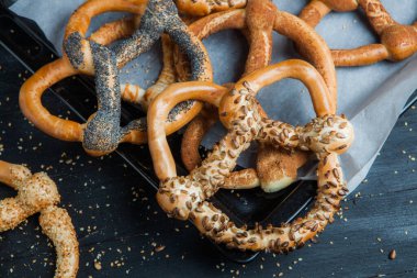 Taze ev yapımı yumuşak krakerler. Siyah arka planda tohumları olan farklı pişmiş simit türleri..