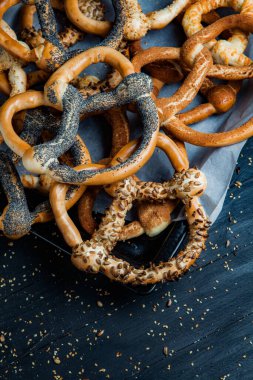 Taze ev yapımı yumuşak krakerler. Siyah arka planda tohumları olan farklı pişmiş simit türleri..