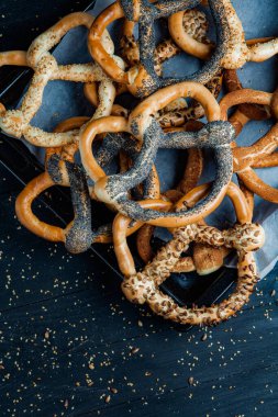 Taze ev yapımı yumuşak krakerler. Siyah arka planda tohumları olan farklı pişmiş simit türleri..