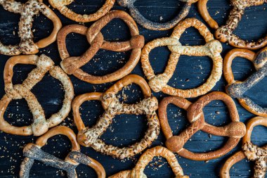 Taze ev yapımı yumuşak krakerler. Siyah arka planda tohumları olan farklı pişmiş simit türleri..