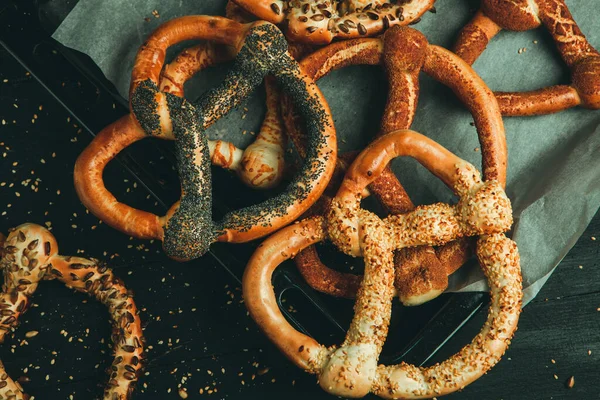 Taze ev yapımı yumuşak krakerler. Siyah arka planda tohumları olan farklı pişmiş simit türleri..