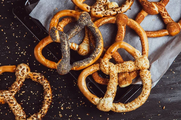 Taze ev yapımı yumuşak krakerler. Siyah arka planda tohumları olan farklı pişmiş simit türleri..