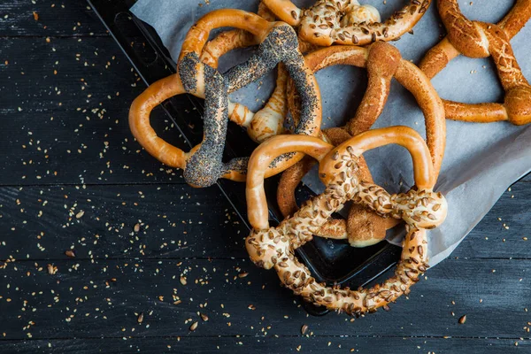 Taze ev yapımı yumuşak krakerler. Siyah arka planda tohumları olan farklı pişmiş simit türleri..