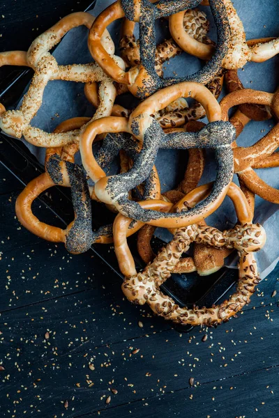 Taze ev yapımı yumuşak krakerler. Siyah arka planda tohumları olan farklı pişmiş simit türleri..