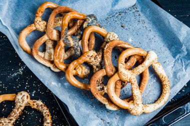 Taze ev yapımı yumuşak krakerler. Siyah arka planda tohumları olan farklı pişmiş simit türleri..