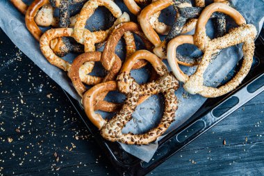 Taze ev yapımı yumuşak krakerler. Siyah arka planda tohumları olan farklı pişmiş simit türleri..