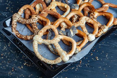 Taze ev yapımı yumuşak krakerler. Siyah arka planda tohumları olan farklı pişmiş simit türleri..