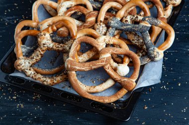 Taze ev yapımı yumuşak krakerler. Siyah arka planda tohumları olan farklı pişmiş simit türleri..