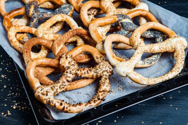 Taze ev yapımı yumuşak krakerler. Siyah arka planda tohumları olan farklı pişmiş simit türleri..