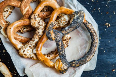 Taze ev yapımı yumuşak krakerler. Siyah arka planda tohumları olan farklı pişmiş simit türleri..