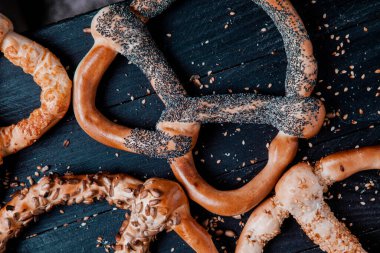 Taze ev yapımı yumuşak krakerler. Siyah arka planda tohumları olan farklı pişmiş simit türleri..