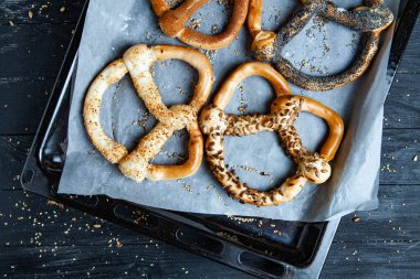 Taze ev yapımı yumuşak krakerler. Siyah arka planda tohumları olan farklı pişmiş simit türleri..