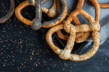 Taze ev yapımı yumuşak krakerler. Siyah arka planda tohumları olan farklı pişmiş simit türleri..