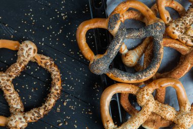 Taze ev yapımı yumuşak krakerler. Siyah arka planda tohumları olan farklı pişmiş simit türleri..