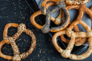 Taze ev yapımı yumuşak krakerler. Siyah arka planda tohumları olan farklı pişmiş simit türleri..