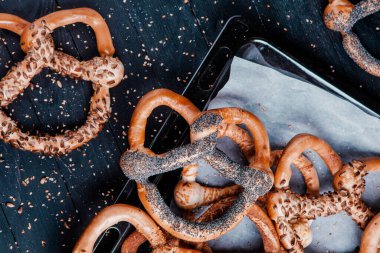 Taze ev yapımı yumuşak krakerler. Siyah arka planda tohumları olan farklı pişmiş simit türleri..