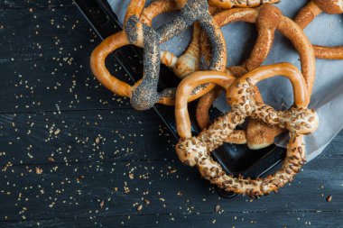 Taze ev yapımı yumuşak krakerler. Siyah arka planda tohumları olan farklı pişmiş simit türleri..