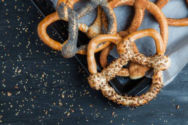 Taze ev yapımı yumuşak krakerler. Siyah arka planda tohumları olan farklı pişmiş simit türleri..