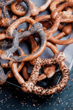 Taze ev yapımı yumuşak krakerler. Siyah arka planda tohumları olan farklı pişmiş simit türleri..