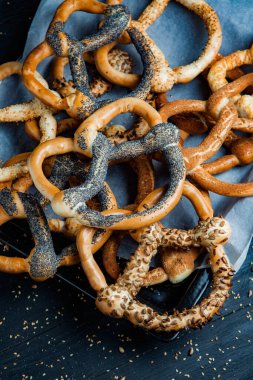Taze ev yapımı yumuşak krakerler. Siyah arka planda tohumları olan farklı pişmiş simit türleri..