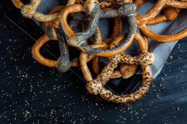 Taze ev yapımı yumuşak krakerler. Siyah arka planda tohumları olan farklı pişmiş simit türleri..