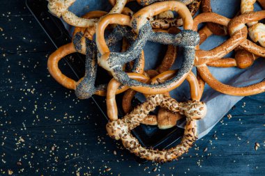 Taze ev yapımı yumuşak krakerler. Siyah arka planda tohumları olan farklı pişmiş simit türleri..