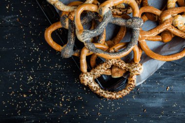 Taze ev yapımı yumuşak krakerler. Siyah arka planda tohumları olan farklı pişmiş simit türleri..