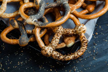 Taze ev yapımı yumuşak krakerler. Siyah arka planda tohumları olan farklı pişmiş simit türleri..