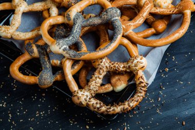 Taze ev yapımı yumuşak krakerler. Siyah arka planda tohumları olan farklı pişmiş simit türleri..