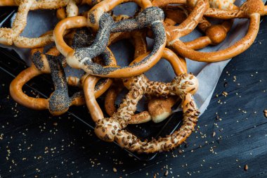 Taze ev yapımı yumuşak krakerler. Siyah arka planda tohumları olan farklı pişmiş simit türleri..