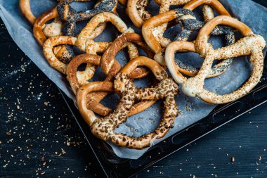 Taze ev yapımı yumuşak krakerler. Siyah arka planda tohumları olan farklı pişmiş simit türleri..