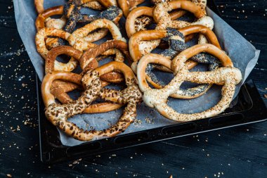 Taze ev yapımı yumuşak krakerler. Siyah arka planda tohumları olan farklı pişmiş simit türleri..