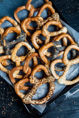 Taze ev yapımı yumuşak krakerler. Siyah arka planda tohumları olan farklı pişmiş simit türleri..