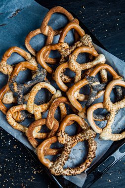 Taze ev yapımı yumuşak krakerler. Siyah arka planda tohumları olan farklı pişmiş simit türleri..