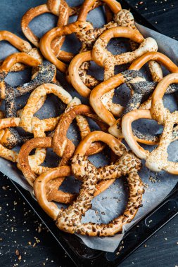 Taze ev yapımı yumuşak krakerler. Siyah arka planda tohumları olan farklı pişmiş simit türleri..