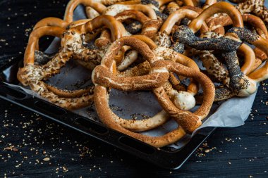 Taze ev yapımı yumuşak krakerler. Siyah arka planda tohumları olan farklı pişmiş simit türleri..