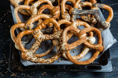 Taze ev yapımı yumuşak krakerler. Siyah arka planda tohumları olan farklı pişmiş simit türleri..