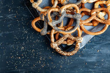 Taze ev yapımı yumuşak krakerler. Siyah arka planda tohumları olan farklı pişmiş simit türleri..