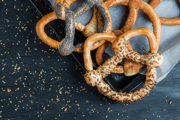 Taze ev yapımı yumuşak krakerler. Siyah arka planda tohumları olan farklı pişmiş simit türleri..