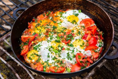 Yumurtalar, ormanda ateşte tavada sebzelerle hazırlandı. Açık ateşte çırpılmış yumurta pişirmek. Doğada kahvaltı. Turist yemeği..
