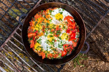 Yumurtalar, ormanda ateşte tavada sebzelerle hazırlandı. Açık ateşte çırpılmış yumurta pişirmek. Doğada kahvaltı. Turist yemeği..