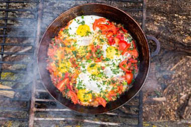 Yumurtalar, ormanda ateşte tavada sebzelerle hazırlandı. Açık ateşte çırpılmış yumurta pişirmek. Doğada kahvaltı. Turist yemeği..